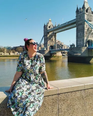A lady sitting on a stone bench in front of Tower Bridge