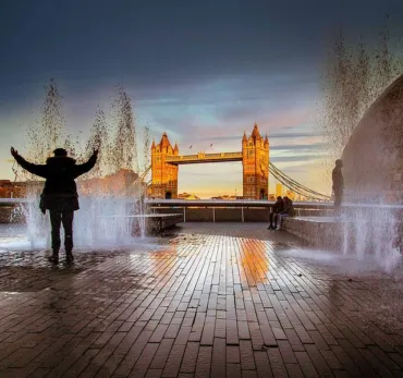 A man posing in front of the fountains with a backdrop of Tower Bridge at sunset.