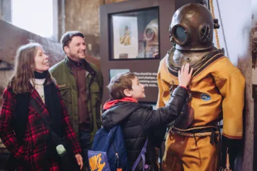 A family interacting with the Diver suit in North Tower level 2 at Tower Bridge