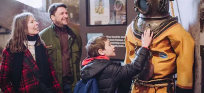 A family interacting with the Diver suit in North Tower level 2 at Tower Bridge