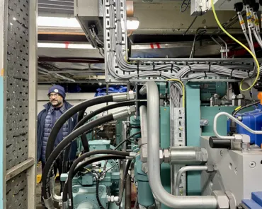 Vijay wearing Tower Bridge uniform standing behind a teal coloured engine with tubes and pipes coming out of it.