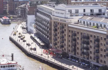 Riverside view of Butler’s Wharf in London from Tower Bridge, featuring historic brick warehouses converted into apartments and restaurants along the River Thames.