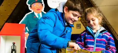Two children holding a piece of paper and the older boy points at it. They are participating in the Tower Bridge Cat Trail
