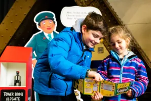 Two children holding a piece of paper and the older boy points at it. They are participating in the Tower Bridge Cat Trail