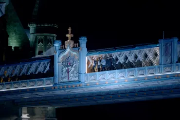 Four men standing on the edge of the High-Level Walkways of Tower Bridge at night.