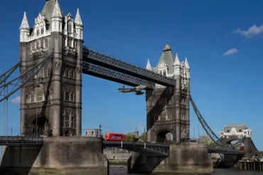 A hyper-realistic painting of a jet plane flyring through Tower Bridge on a sunny day.
