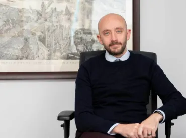 A man sitting in an office, with a framed drawing in the background