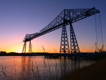 A silhousette of a large towering steel structure of a bridge over sunset.