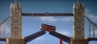 Toy model of Tower Bridge with its bascules raised, and a miniature double-decker bus painted with a Union Jack design positioned between the open sections. The scene is set against a bright blue sky, and is a screenshot of a playful moment from Spice World: The Movie.