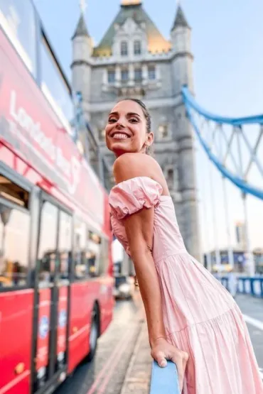 A lady posing in front of Tower Bridge, with a red bus passing by