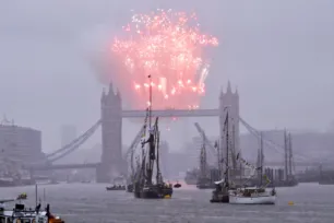 Fireworks explode above the walkways over Tower Bridge, with tall ships in the foreground