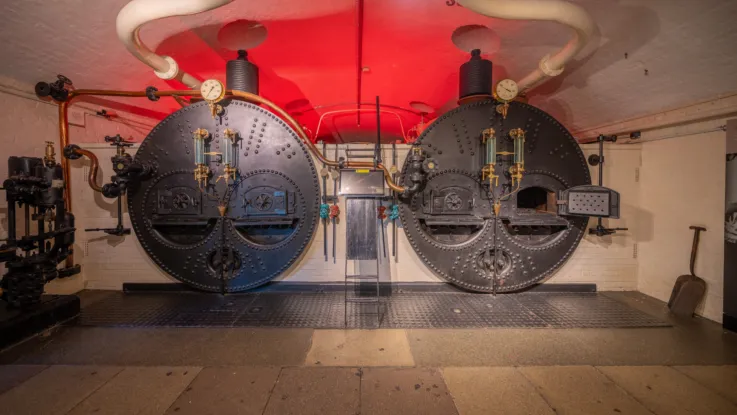 Two large black cylindrical coal-fired boilers inside Tower Bridge’s historic engine rooms in London.